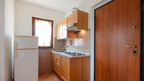 Une cuisine de taille réduite, équipée d’un réfrigérateur, d’une cuisinière, de meubles de rangement en bois et d’une fenêtre.