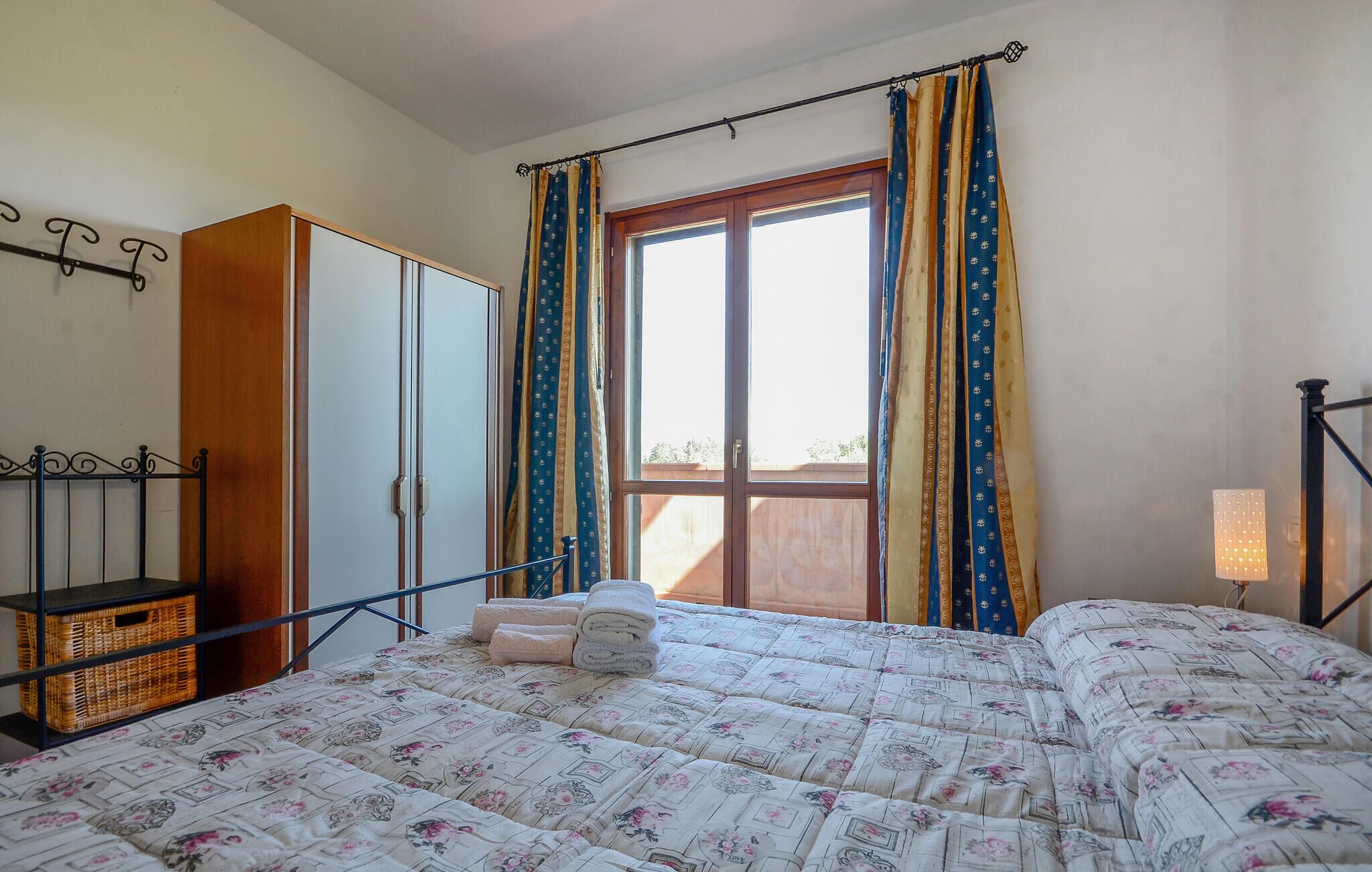 A bedroom with a bed, a wardrobe, a window with curtains, a bedside lamp, and a balcony.