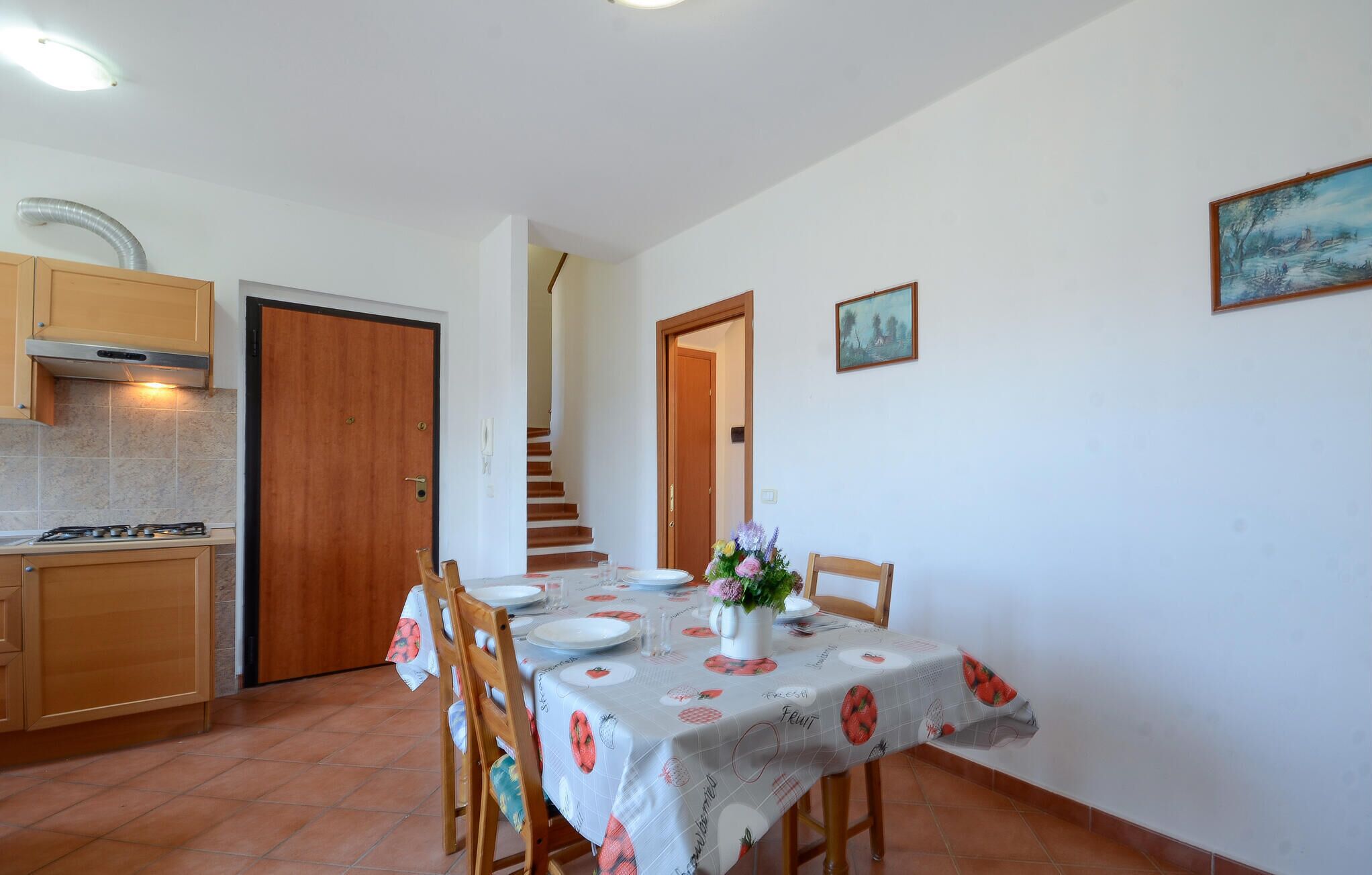 A dining area with a table set for four, a kitchen with a stove, and a staircase leading to another level.