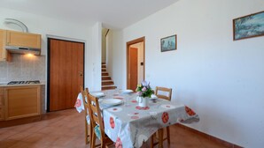 Un coin repas avec une table dressée pour quatre personnes, une cuisine équipée d’une cuisinière et un escalier menant à un autre niveau.