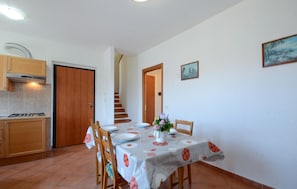 A dining area with a table set for four, a kitchen with a stove, and a staircase leading to another level. - 3 bedroom stunning apartment in Pomonte (Pomonte)
