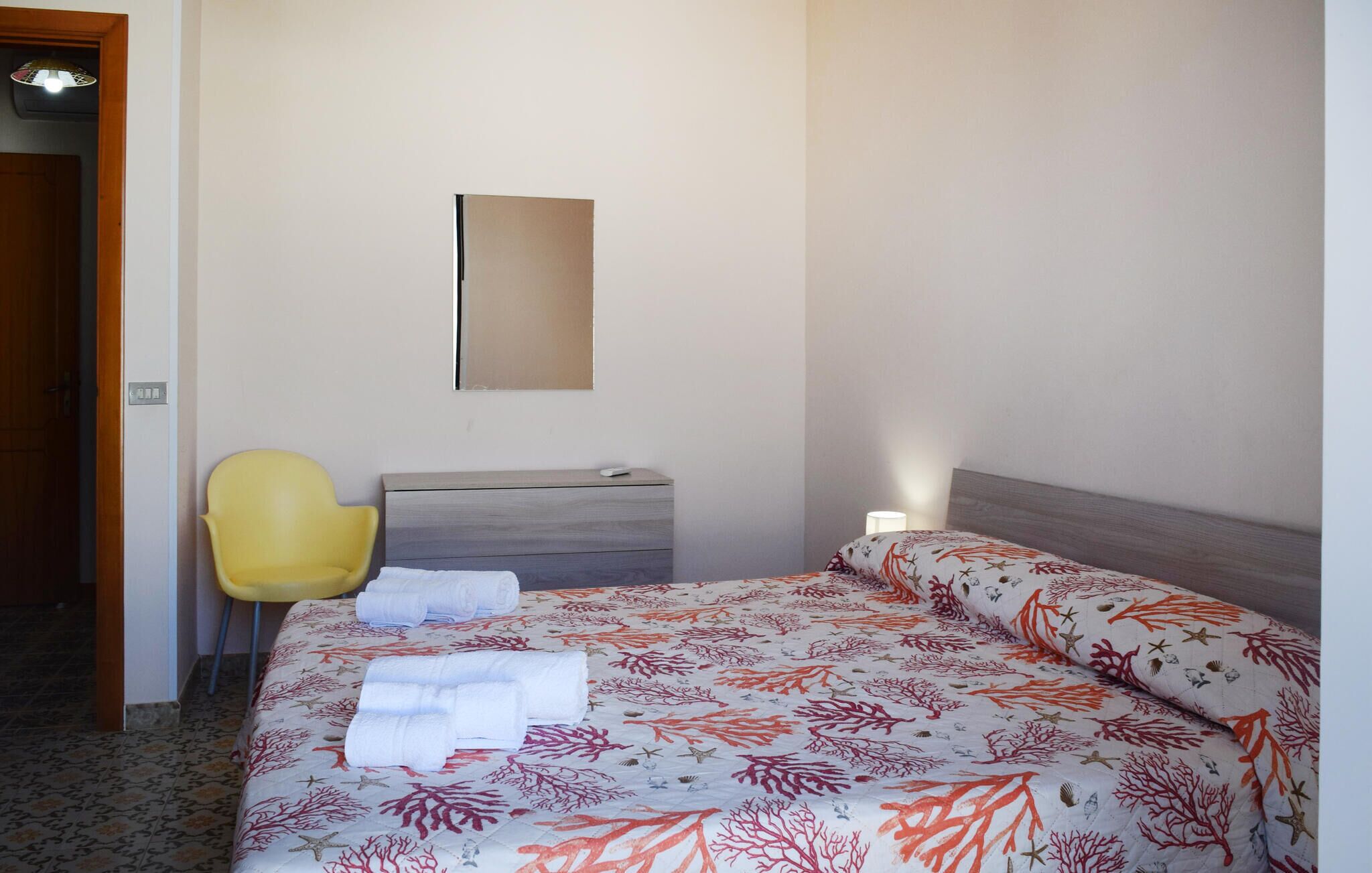 A hotel room with a bed, a chair, a bedside table, and a mirror on the wall.