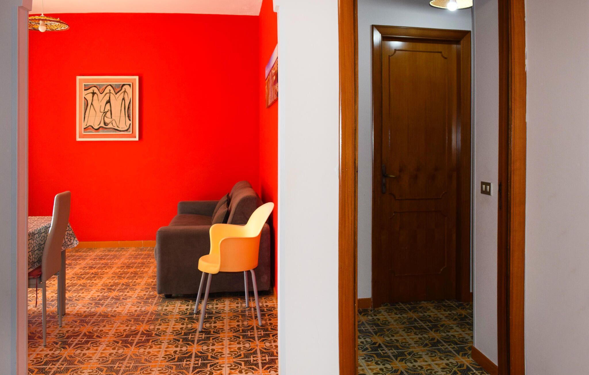 A room with a red wall, a patterned floor, a brown sofa, a yellow chair, and a wooden door.