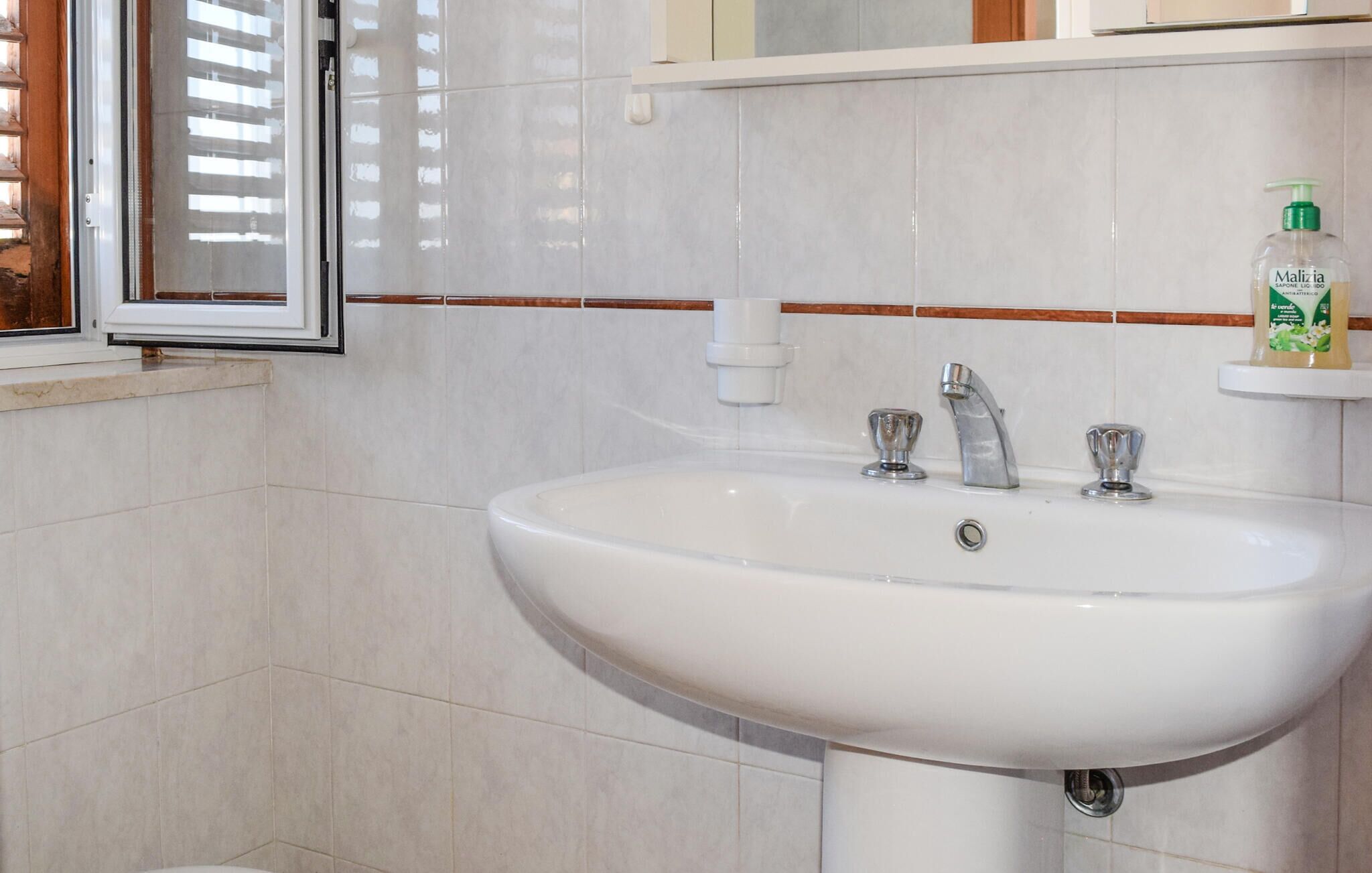 A bathroom with a white sink, two faucets, and a window with blinds.