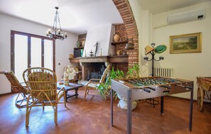 Ein gemütliches Wohnzimmer mit Kamin aus Backsteinen, Korbstühlen, einem Tischkicker und einer Hängelampe.