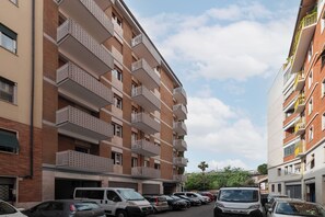 A multi-story residential building with balconies, a parking area, and a clear sky.