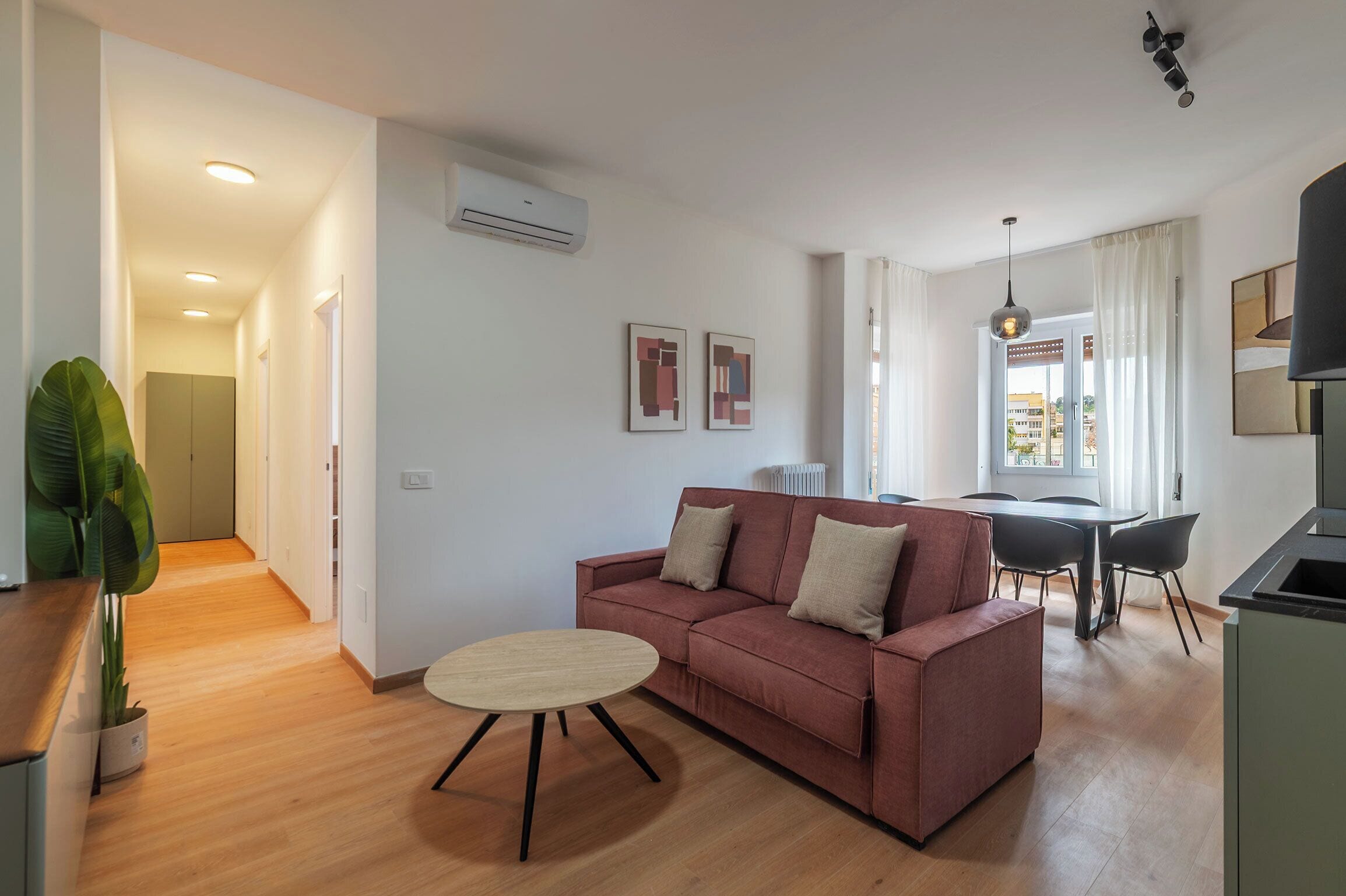 A modern living room with a sofa, a dining table, and a kitchen area.