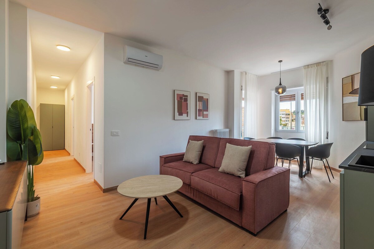 A modern living room with a sofa, a dining table, and a kitchen area.