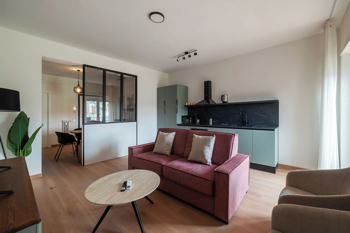 A modern living room with a sofa, a round coffee table, and a kitchen area with a black countertop and cabinets.