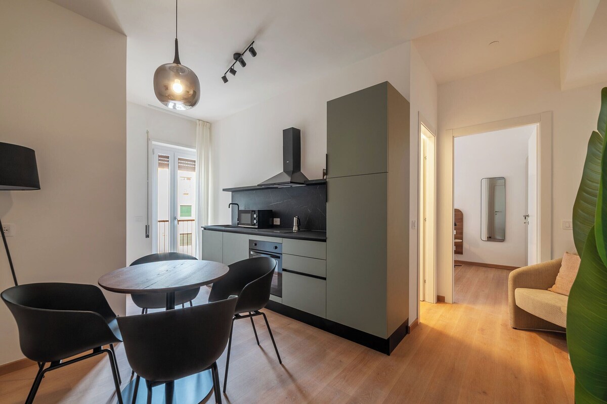 A modern kitchen with a dining area, a sofa, and a large plant.
