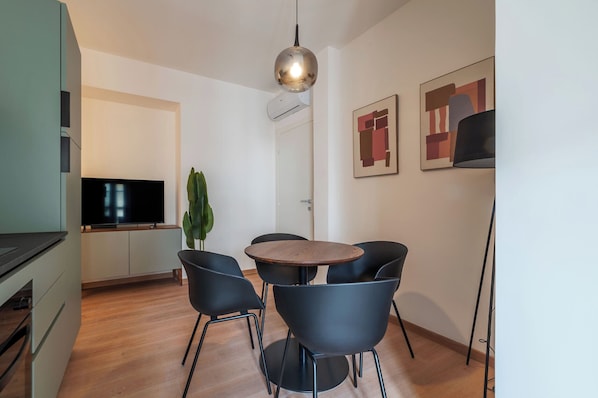A modern kitchen with a flat-screen TV, a dining table with four chairs, and a pendant light. - Stylish Balcony Flats by the Vatican (Roma)