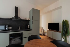 A modern kitchen with a microwave, stove, and cabinets, a dining area with a table and chairs, and a TV on a stand. - Stylish Balcony Flats by the Vatican (Roma)