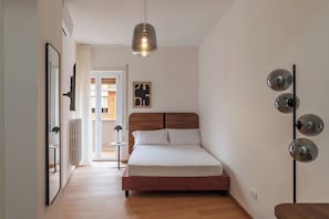 A bedroom with a wooden bed, a hanging pendant light, a wall-mounted light fixture, and a door leading to a balcony. - Stylish Balcony Flats by the Vatican (Roma)