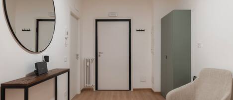 A hallway with a wooden floor, a round mirror, a desk with a laptop, a door, and a green cabinet.