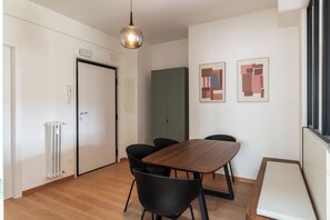 Ein Zimmer mit Holztisch, schwarzen Stühlen, einer Heizung, einer Tür und abstrakter Kunst an der Wand.