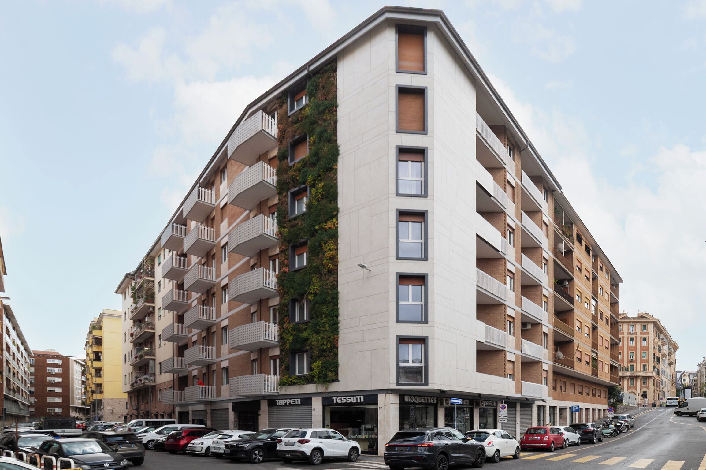 A multi-story building with balconies, a green vertical garden, and storefronts with signage.