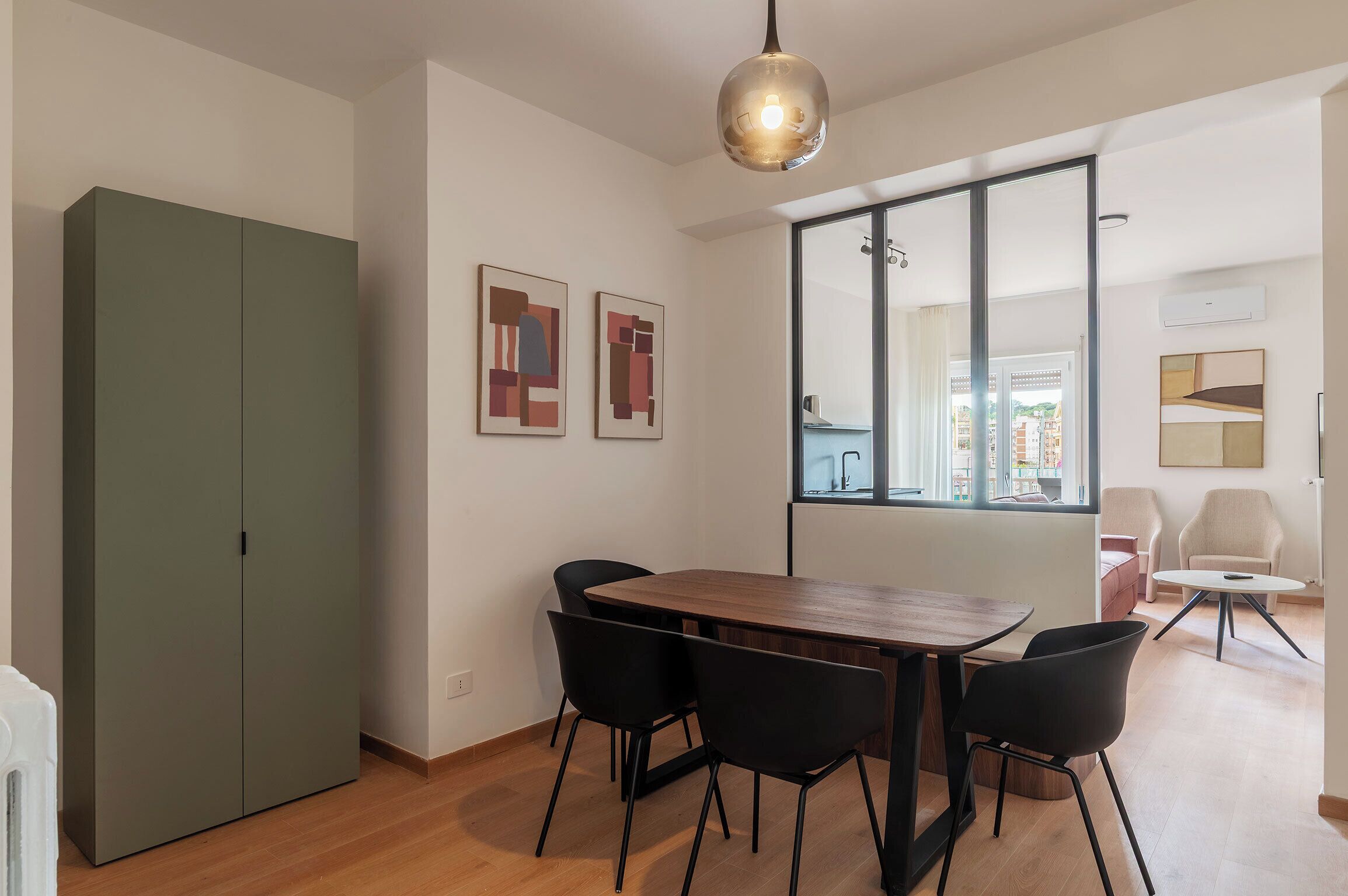 Un'area pranzo moderna con un tavolo in legno, sedie nere, un'armadiatura verde e arte astratta alle pareti.