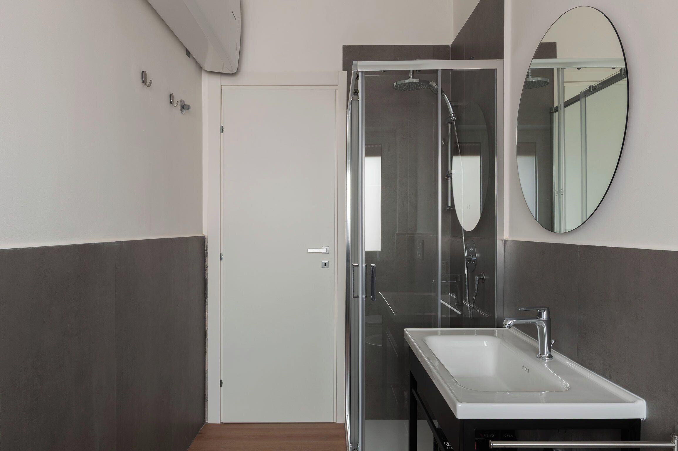 A bathroom with a glass shower enclosure, a white sink, and a round mirror on the wall.