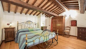 A bedroom with a wooden ceiling, a bed with ornate metal headboard, a wooden wardrobe, and a chair. - Amazing apartment in Frazione Montebibico (Frazione Montebibico)