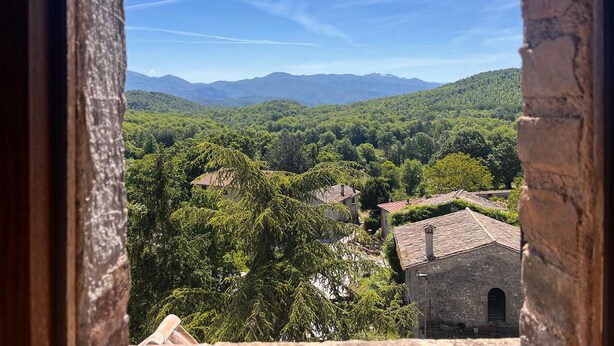 A view through a window of a rural landscape with mountains in the distance, a few buildings, and dense greenery. - Amazing apartment in Frazione Montebibico (Frazione Montebibico)