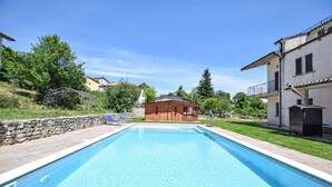A swimming pool with a stone wall and lounge chairs, surrounded by houses and greenery. - Amazing apartment in Frazione Montebibico (Frazione Montebibico)