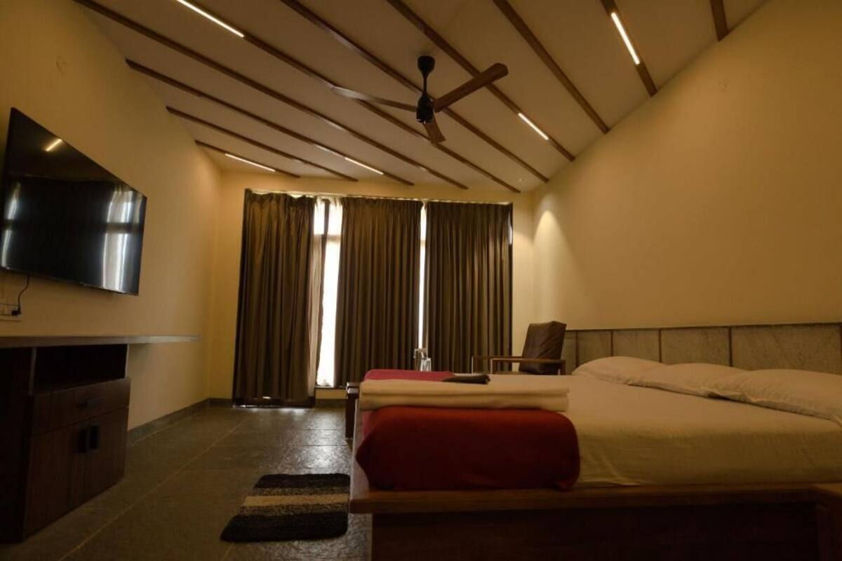 Una habitación de hotel con cama, televisión, ventilador de techo y ventana con cortinas.