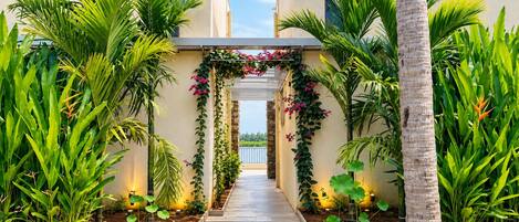 A pathway flanked by lush greenery and a decorative archway with flowering vines.