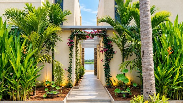A pathway flanked by lush greenery and a decorative archway with flowering vines.