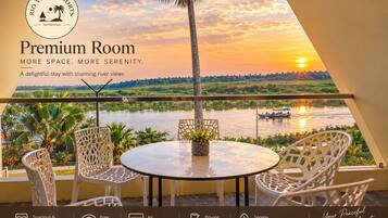 Habitación premium con balcón que da al río, con una mesa y sillas, y vistas al atardecer.