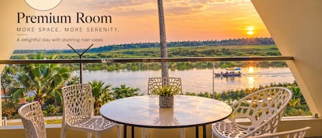 A premium room with a balcony overlooking a river, featuring a table and chairs, and a view of the sunset.