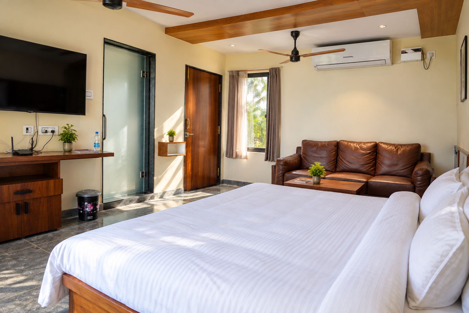 A hotel room with a large bed, a desk with a computer, a television, and a leather sofa.