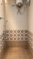 Zona de ducha con cabezal de ducha de mano, cabezal de ducha instalado en la pared y calentador de agua.