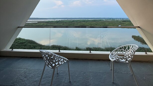 A room with a large triangular window overlooking a landscape, two white chairs, and a tiled floor. - Rio Vista (Razole)