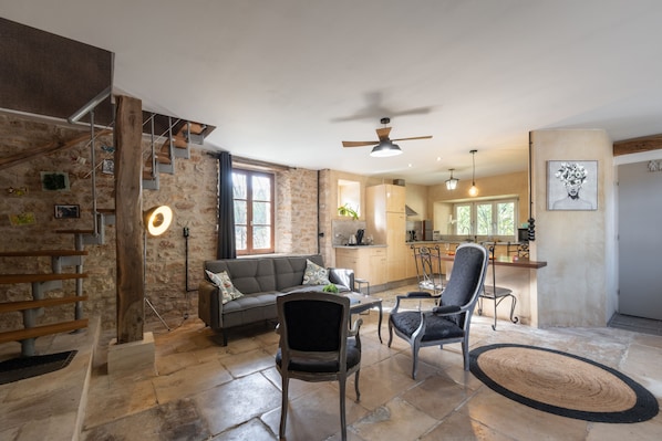 A spacious living area with a stone wall, a staircase, a sofa, and a dining area with chairs and a table.