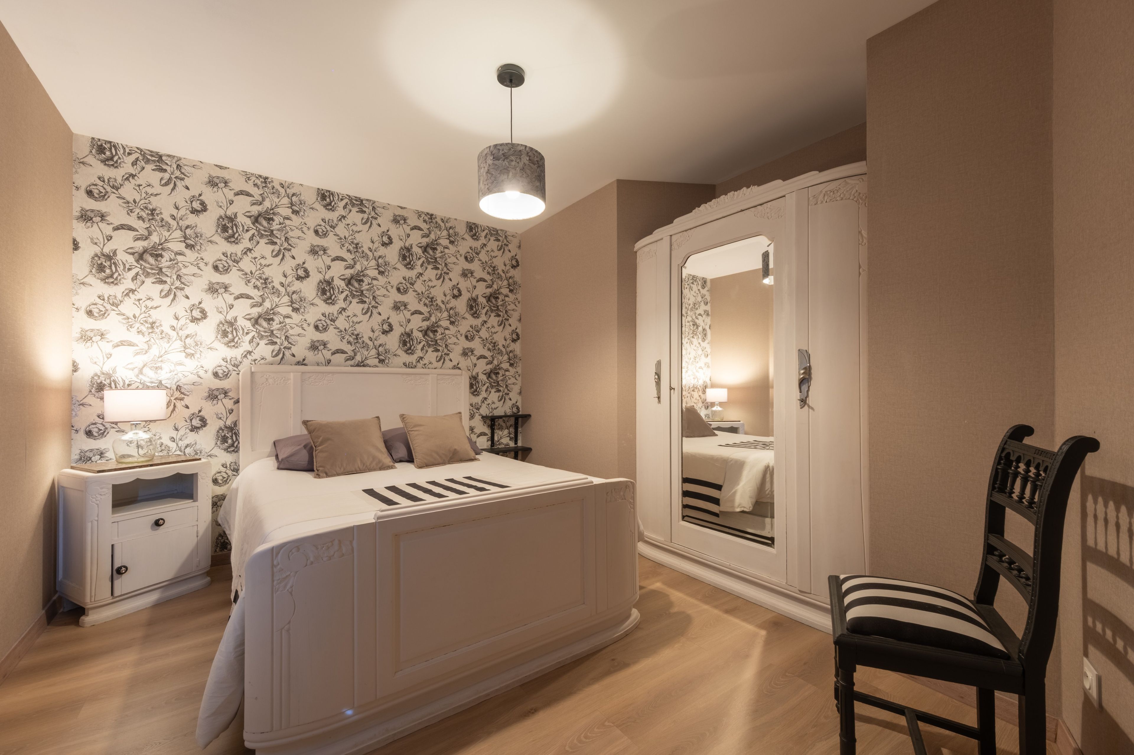 Ein Schlafzimmer mit Bett, Nachttisch, Stuhl, Kleiderschrank und Spiegel.