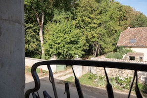 A view of a rural road with a stone wall and a green gate, leading to a house with a tiled roof and a small window.