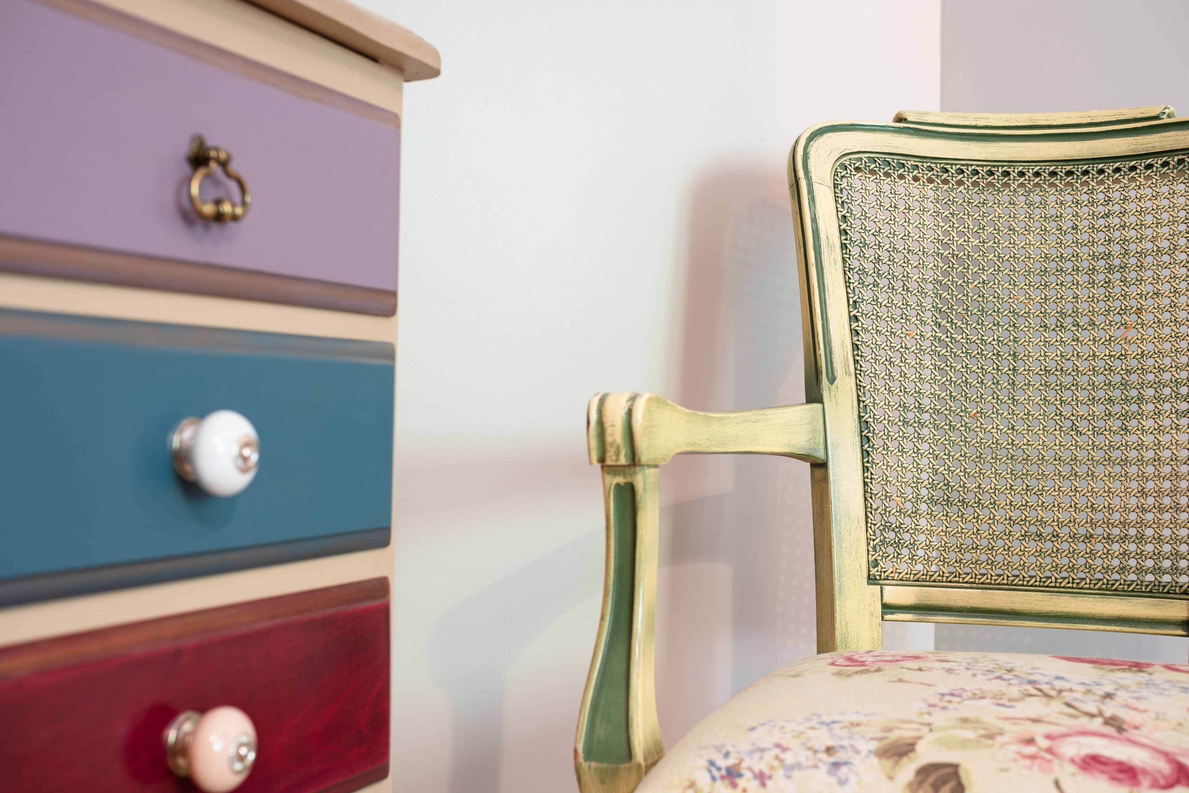 Una silla de estilo vintage con respaldo y reposabrazos trenzados, ubicada junto a un aparador con varios cajones y una aldaba decorativa.