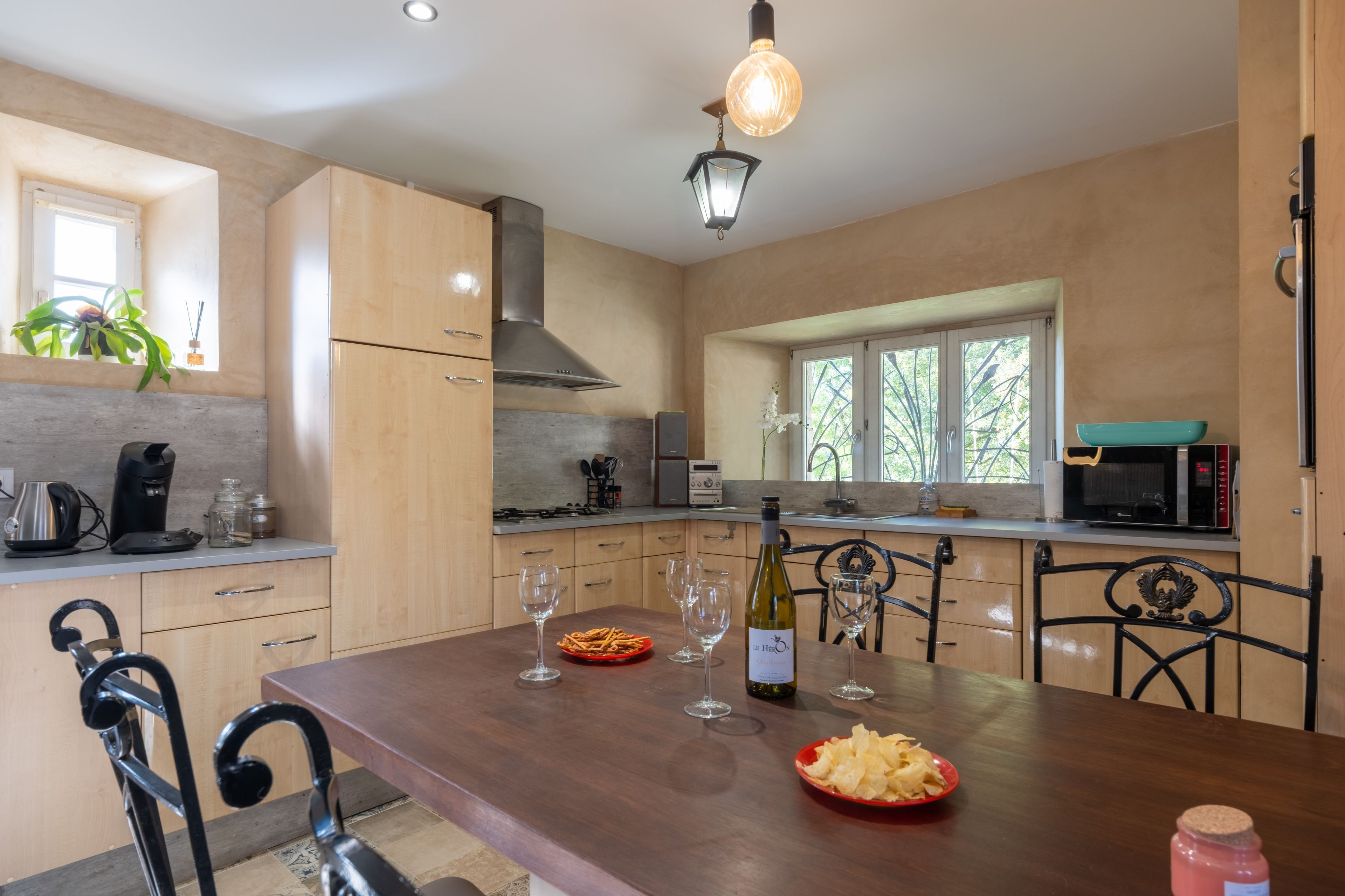 A modern kitchen with wooden cabinets, a dining table set with wine glasses and plates, and a bottle of wine.