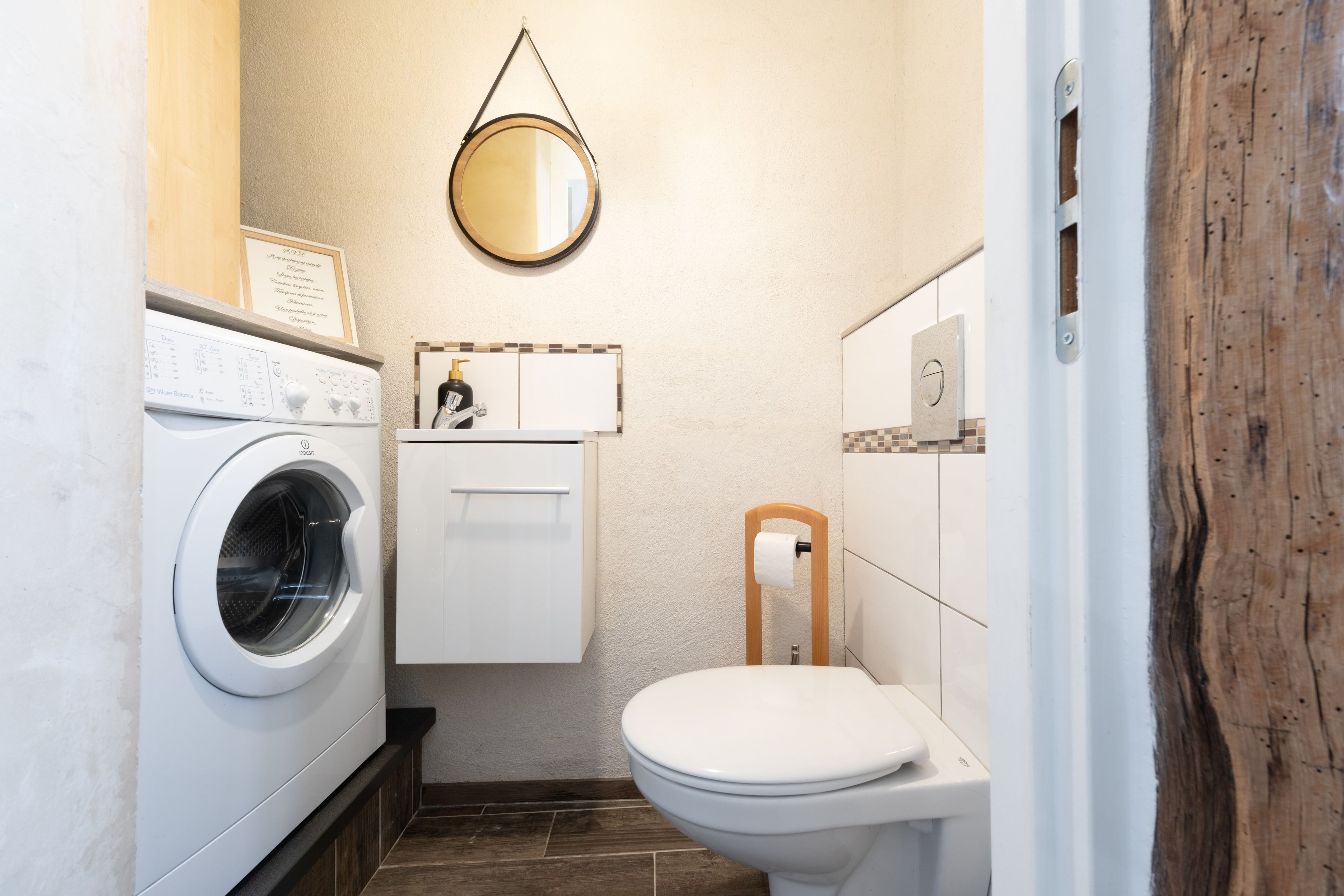 A compact bathroom with a washing machine, a toilet, and a mirror.