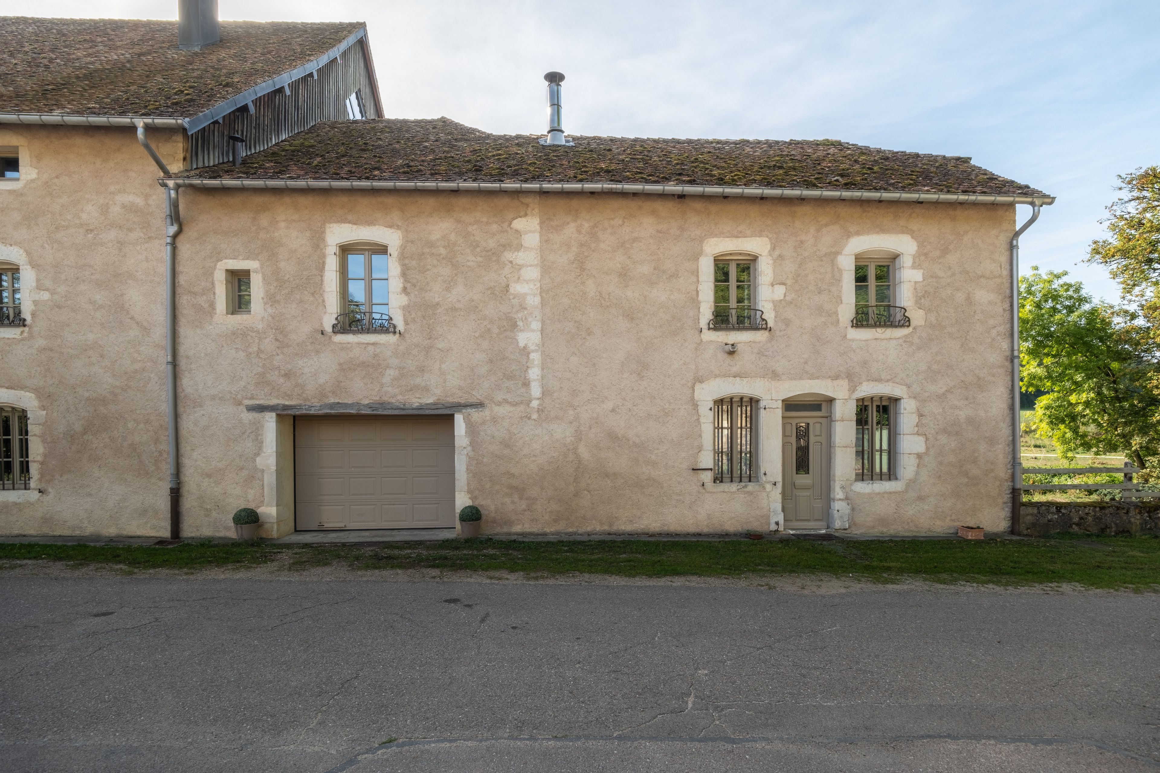 Un bâtiment à deux étages doté d’une porte de garage, de nombreuses fenêtres avec volets et d’une cheminée.