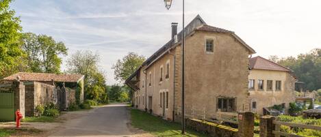Un camino rural que conduce a un edificio tradicional de piedra con techo de tejas, una farola y una verja verde.