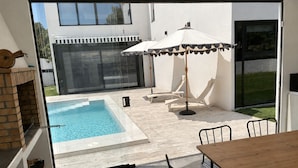 Eine moderne Terrassenanlage mit Pool, Esstisch und Grill.