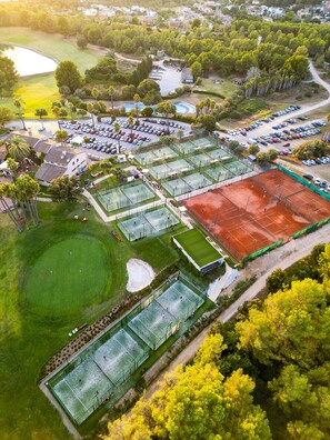 Eine Vogelperspektive eines Sportkomplexes mit mehreren Tennisplätzen, einem Parkplatz und umgebender Grünfläche.