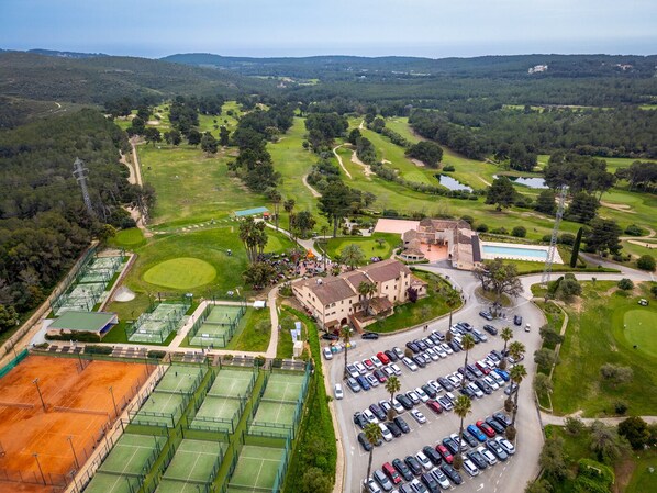 Eine Vogelperspektive auf einen Golfplatz mit mehreren Tennisplätzen, einem Parkplatz und einem Gebäude mit Schwimmbad.