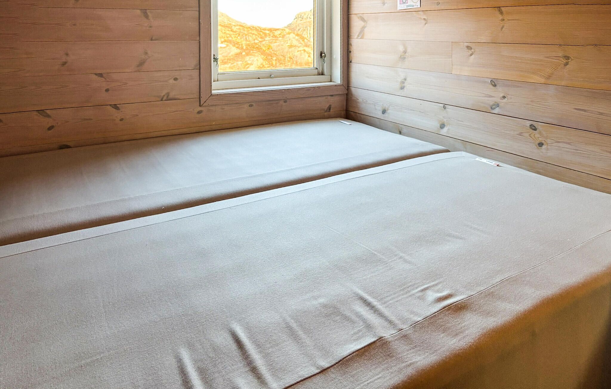 Ein Zimmer mit Holzbalkendecke, einem Fenster und einem Bett mit weißer Matratze.