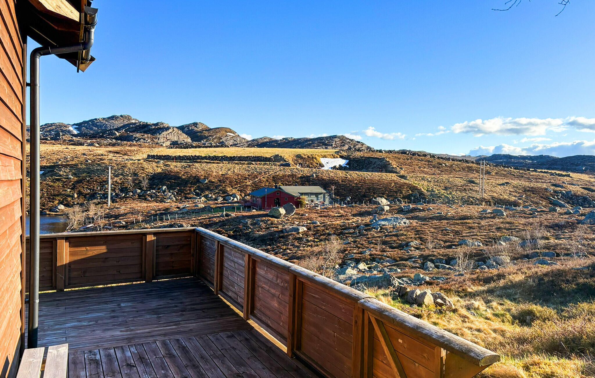 A wooden deck with a view of a mountainous landscape, a small red building, and a clear sky.
