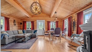 L’intérieur d’une cabane en rondins, avec un canapé, une table à manger, des chaises, une cheminée et un luminaire au plafond.