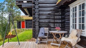 Une cabane en bois dotée d’une terrasse, d’un foyer et d’une table avec des chaises.
