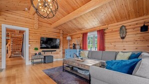 L’intérieur d’une cabane en rondins, avec un plafond en bois, un téléviseur, un canapé et un coin repas.