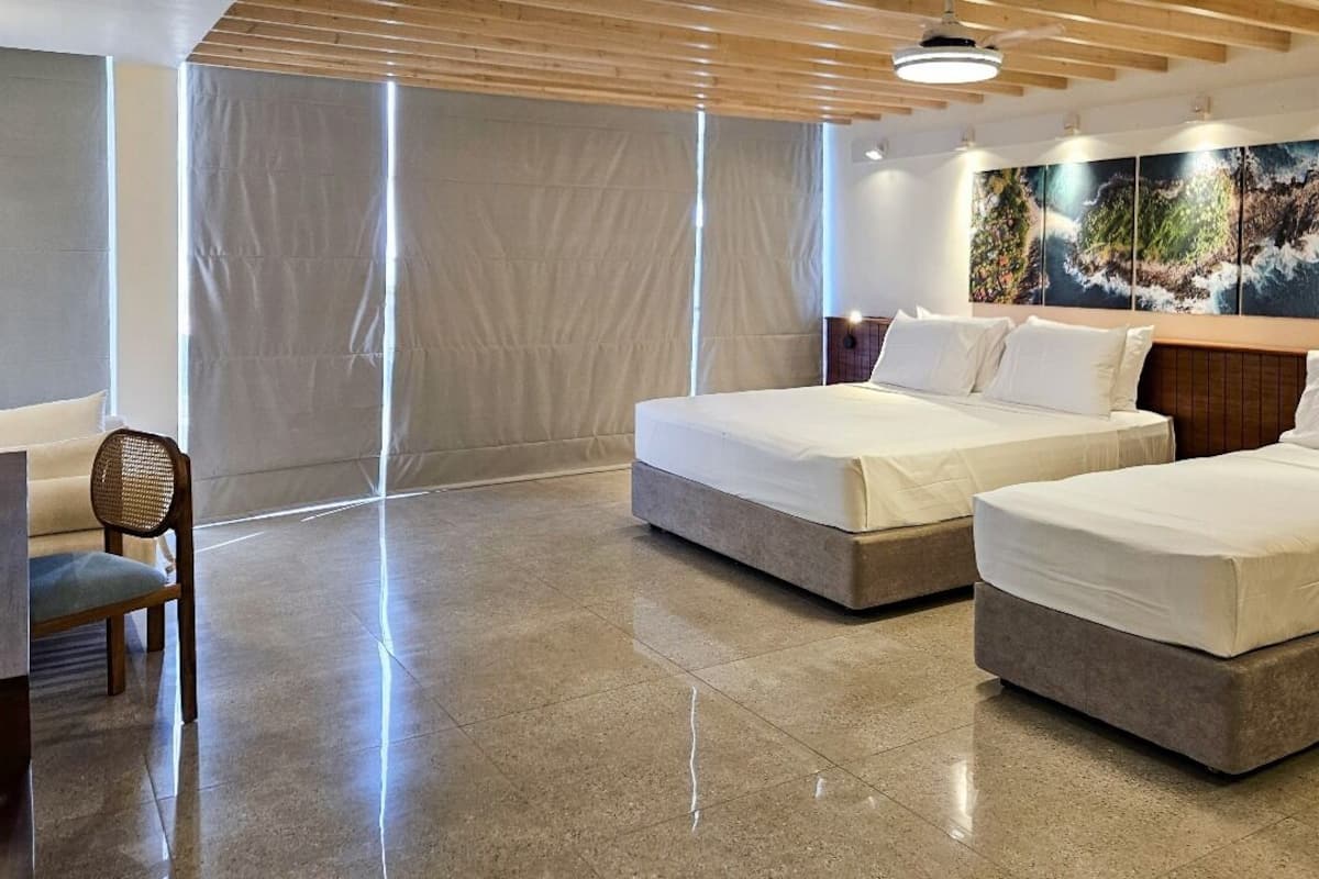 A hotel room with two beds, a chair, and a large window with curtains.